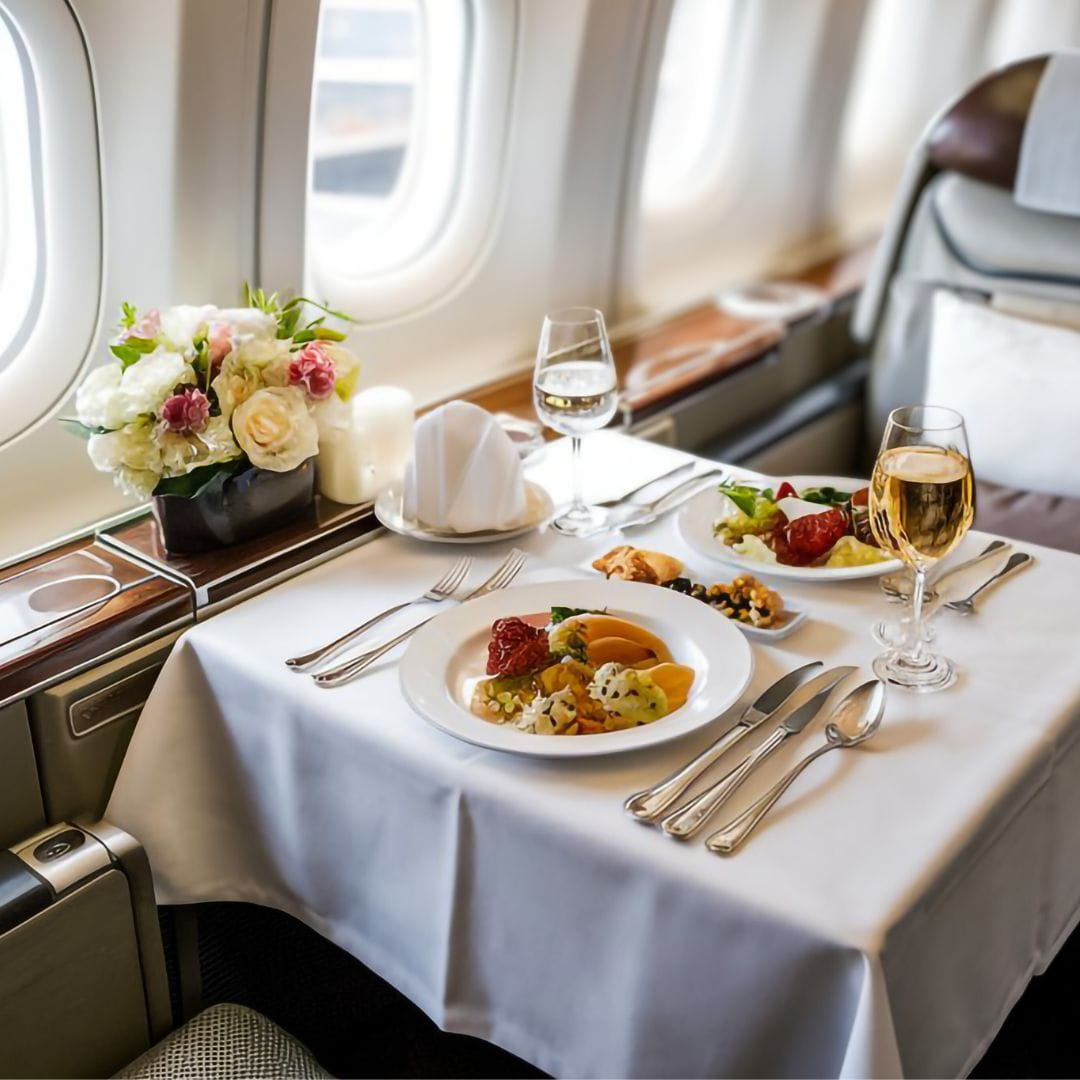 Private jet dining table elegantly set with champagne flutes, gourmet dishes and a floral bouquet for in-flight catering.